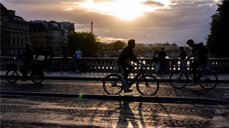 Menschen fahren bei Sonnenuntergang mit dem Fahrrad auf einer Brücke über die Seine in Paris.