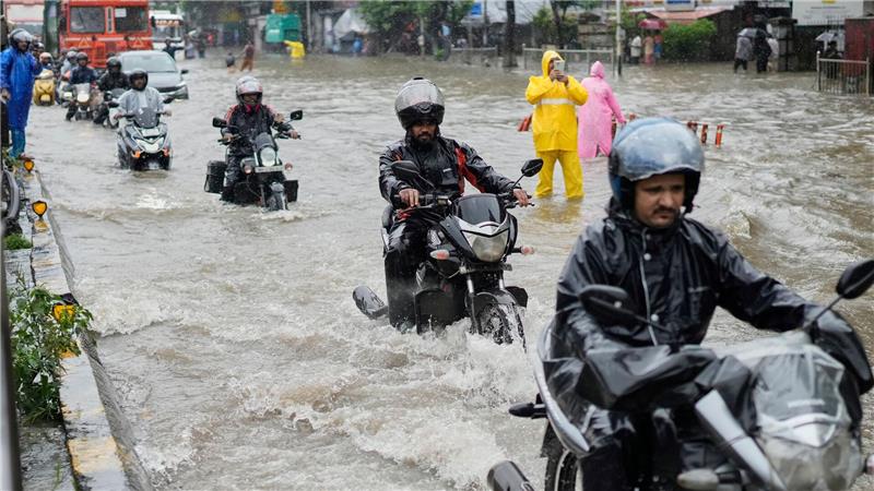 Bilder des Tages Menschen fahren bei starkem Regen in Mumbai mit Motorrädern durch eine überschwemmte Straße.