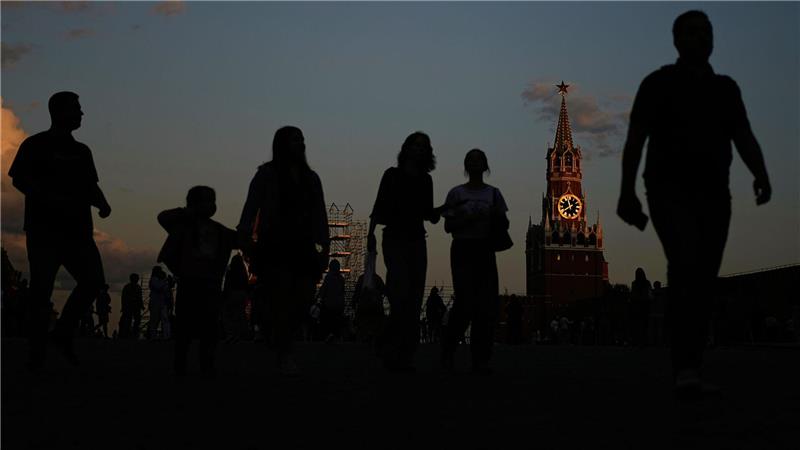 Menschen gehen über den Roten Platz, während das Sonnenlicht von der Kreml-Uhr auf dem Spasskaja-Turm des Kremls reflektiert wird.