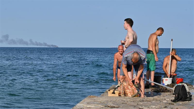 Schwarzes Meer: Bedroht der Seekrieg den Getreidehandel? Menschen in Odessa sonnen sich, während am Horizont im Schwarzen Meer der brennende Getreidetransporter „Golden Leo“ zu sehen ist. (Archivbild)