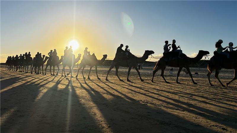 Menschen reiten auf Kamelen am Birubi Beach nördlich von Newcastle in Australien.