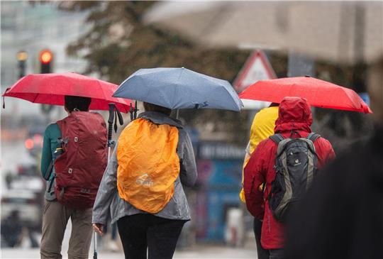 Menschen schützen sich bei Regen mit ihren Schirmen.
