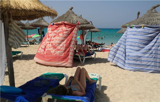 Menschen schützen sich bei heißen Temperaturen mit Strandtüchern vor der Sonne am Strand von Arenal.