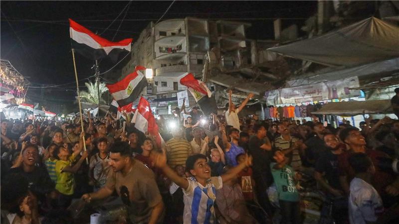 Menschen schwenke agyptische Flaggen und verfolgen im zentralen Gazastreifen das WM-Spiel Ägypten gegen Belgien auf einer Großbildleinwand.