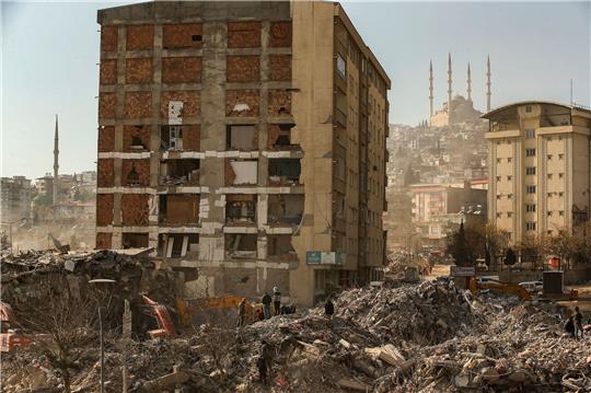 Menschen stehen im türkischen Kahramanmaras vor einem eingestürzten Gebäude.