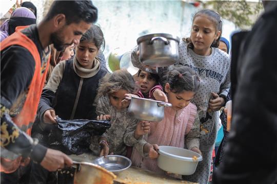 Menschen stehen in Rafah im Süden des Gazastreifens mit Töpfen, Schalen und Tüten bei einer Essensausgabe an.
