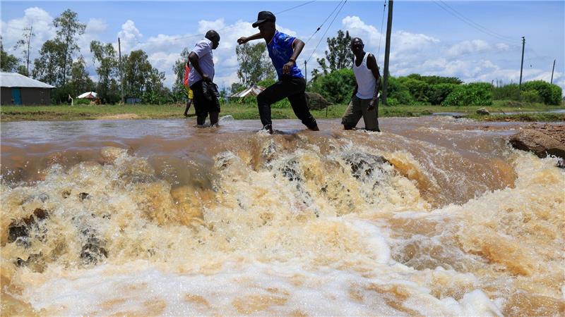 Menschen überqueren einen überfluteten Straßenabschnitt nach schweren Regenfällen in Ahero, Kenia.