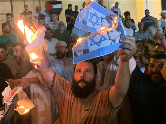 Menschen verbrennen Fotos, die den israelischen Außenminister Eli Cohen und seine libysche Amtskollegin Nadschla al-Mankusch zeigen. In Libyen ist es in der Nacht zum Montag zu gewaltsamen Protesten gekommen.