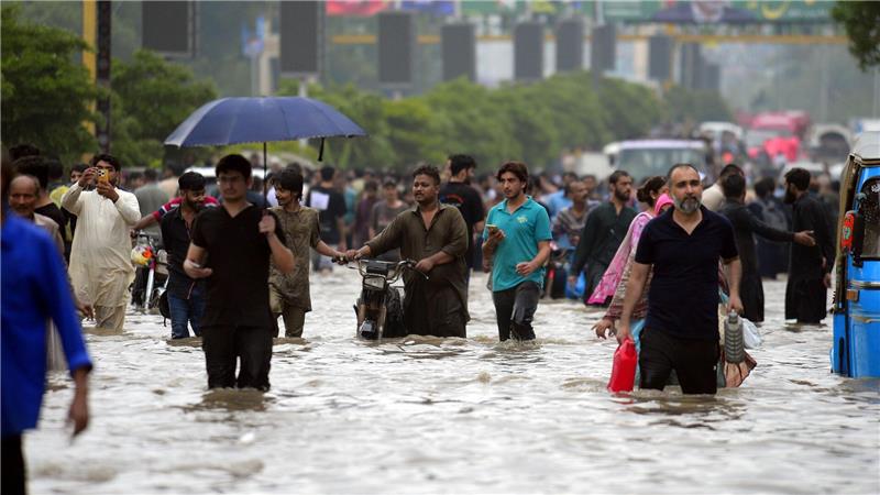 Menschen waten durch eine überflutete Straße nach starkem Monsunregen in Pakistan.