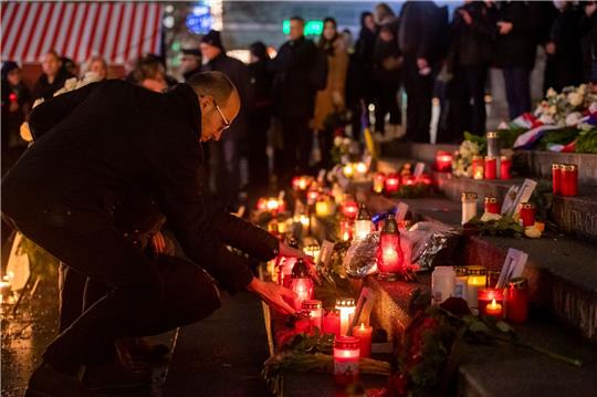 Menschen zünden bei der Gedenkveranstaltung zum Terroranschlag auf dem Berliner Breitscheidplatz an der Gedächtniskirche Kerzen an.