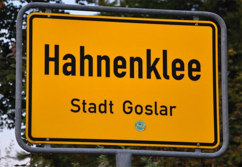 Gelbes Ortsschild mit schwarzer Aufschrift ' Hahnenklee - Stadt Goslar' an einem Metallrahmen 