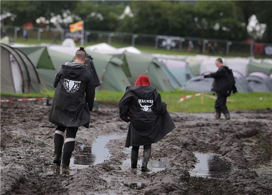 Metal-Fans sind auf dem schlammigen Festivalgelände unterwegs.