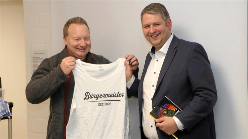 Das Foto zteigt, wie Michael Petrick am Wahlabend ein T-Shirt mit Aufschrift "Bürgermeister" an Martin Schulze erreicht. 