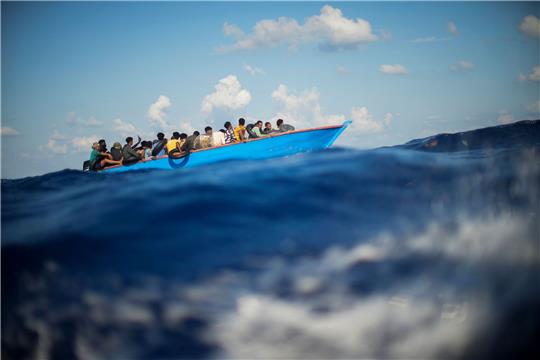 Migranten sitzen in einem Holzboot südlich der italienischen Insel Lampedusa auf dem Mittelmeer.
