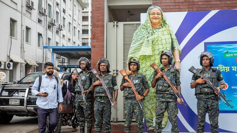 Medien: Fast 100 Tote bei Unruhen in Bangladesch Militärangehörige stehen vor einem großen Porträt von Premierministerin Sheikh Hasina. Sie gilt als autokratisch regierende Premierministerin.