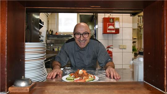 Mimmo Carrozzo steht in der Restaurantküche. Vor ihm steht ein Teller mit Essen auf dem Tisch.