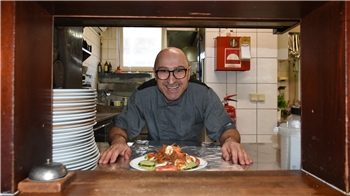 Mimmo Carrozzo steht in der Restaurantküche. Vor ihm steht ein Teller mit Essen auf dem Tisch.