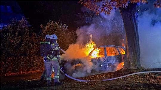 Mit Atemschutz gehen Feuerwehrleute gegen die Flammen vor. Das Auto brennt völlig aus.