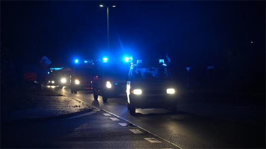 Das Bild zeigt einen nächtlichen Konvoi mehrerer Einsatzfahrzeuge auf einer Straße. Im Vordergrund fährt ein Einsatzfahrzeug mit eingeschaltetem blauen Blaulicht, dahinter folgen weitere Fahrzeuge mit eingeschalteter Warn- und Beleuchtungstechnik. Die Aufnahme entstand bei Dunkelheit an einer Kreuzung beziehungsweise Einmündung und vermittelt durch die Beleuchtung und die Fahrbewegung eine typische Einsatzfahrt.