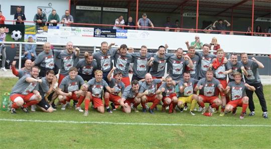 Gruppenfoto einer Fußballmannschaft in grauen Trikots und roten Hosen auf dem Spielfeld vor einer Tribüne mit Zuschauern