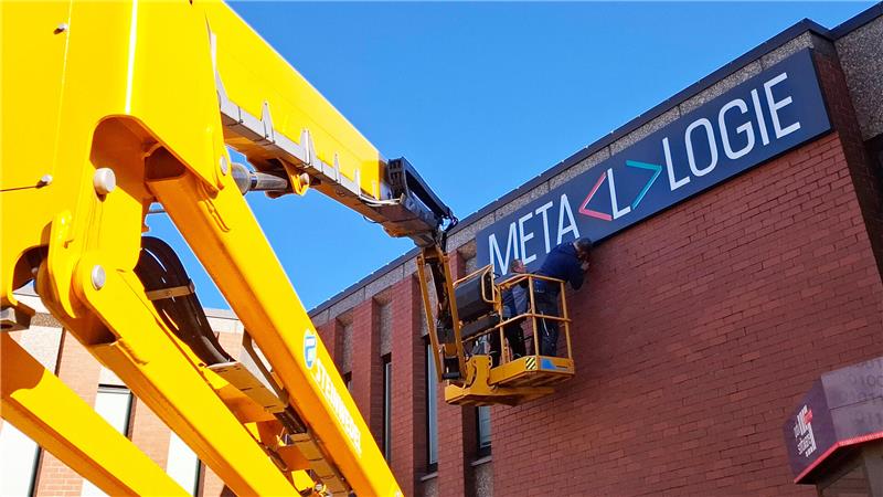 Mit Hubwagen und langem Arm wird das neue Schild am Firmensitz montiert.
