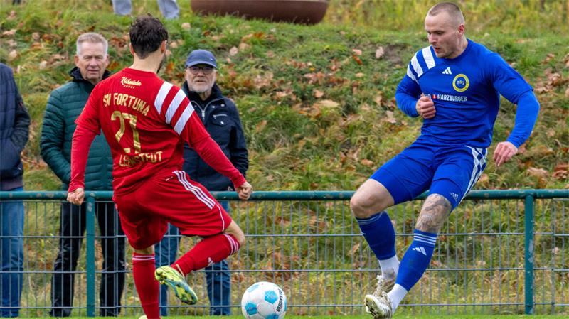 Zwei Fußballspieler in Aktion, einer in rotem Trikot mit der Nummer 21, der andere in blauem Trikot, beide vor einem Fußball auf dem Spielfeld
