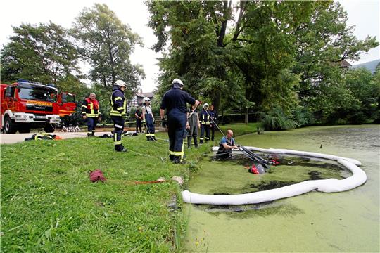 Mit Wathose und Ölschlauchbarriere: Ein Feuerwehrmann holt den versenkten Roller an Land, während der Schlauch Sprit und Schmierstoffe zusammenhalten soll.