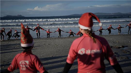 Mit Weihnachtsmannmützen verkleidete Menschen surfen während der „Papanoelada Surfera“ (Surfer-Nikolaus-Aktion) am Strand von Patos. 