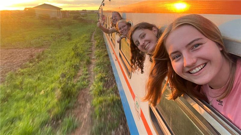 Goslarerin Amalia Saupe trainiert Mädchenteam in Afrika (Teil 2) Mehrere Personen lehnen aus den Fenstern eines fahrenden Zuges bei Sonnenuntergang über eine grüne Landschaft.