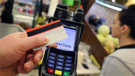 Hand hält eine Kreditkarte vor ein Kartenlesegerät mit beleuchtetem Display.