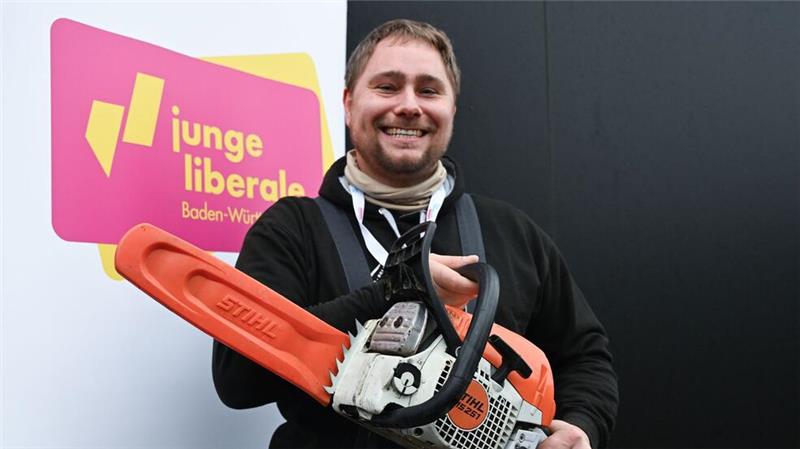 Mit der Kettensäge will Mark Hohensee, Landesvorsitzender der Jungen Liberalen, packt für den Bürokratieabbau symbolisch die Kettensäge aus. 