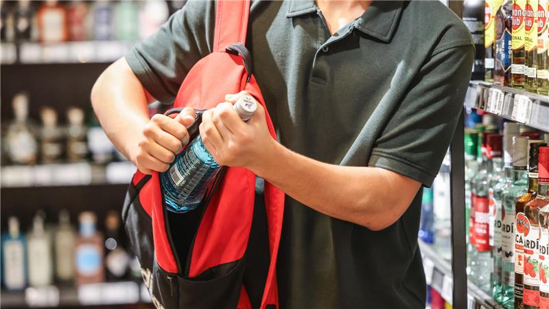 Symbolbild: Ein Mann steckt in einem Supermarkt eine Flasche mit einem alkoholhaltigen Getränk in seinen Rucksack. 