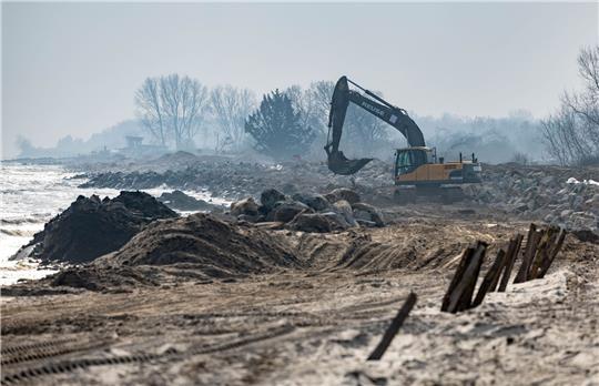 Mit einem Bagger werden große Steine am Strand am Hafen von Damp verladen.