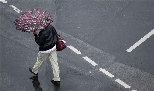 Mit einem Schirm schützt sich eine Passantin vor dem Regen.