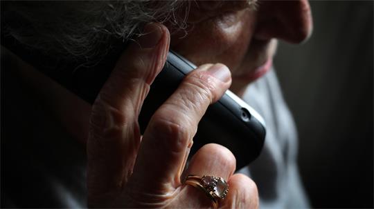 Eine ältere Frau hält sich ein Telefon ans Ohr.