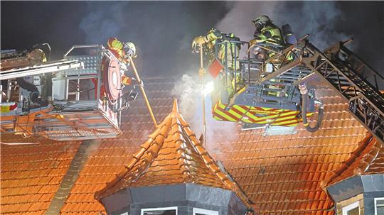 Einsatzkräfte der Feuerwehr arbeiten mit zwei Drehleitern am Dach des betroffenen Hauses.