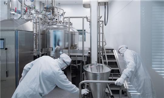 Mitarbeiter eines Pharmaunternehmens arbeiten in einem Reinraum an einer Gelmischanlage.