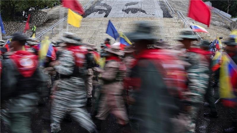 Mitglieder der Bolivarischen Miliz marschieren vor einer Treppe in Caracas, auf der die Augen des verstorbenen Präsidenten Hugo Chavez abgebildet sind, während einer Demonstration zum Gedenken an den Jahrestag der Schlacht von Santa Ines, die während des venezolanischen Bundeskriegs im 19. Jahrhundert stattfand.
