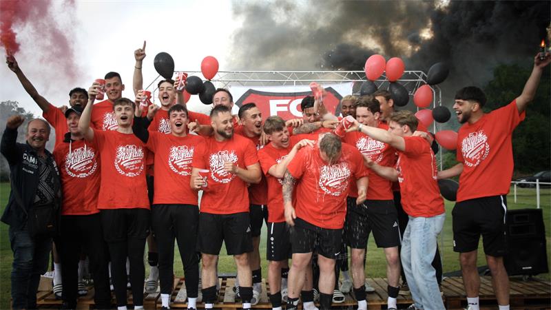 Gruppe jubelnder Männer in roten T-Shirts mit schwarzen und roten Luftballons vor rauchendem Hintergrund