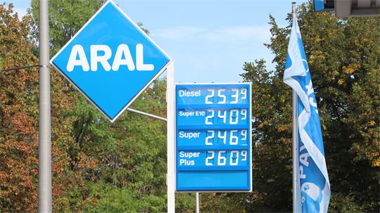 Tankstelle mit ARAL-Logo und Preistafel für Diesel, Super E10, Super und Super Plus vor Bäumen und blau-weißen Fahnen.