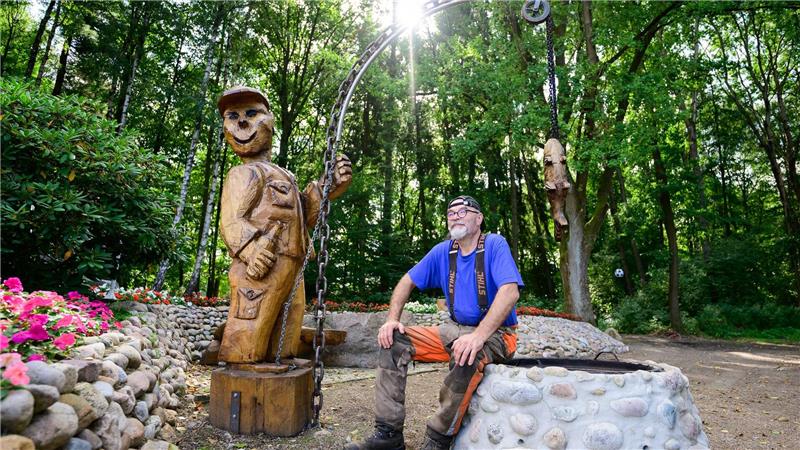 Motorsägenkünstler Andree Löbnitz neben einer Holzskulptur, die er aus einem Holzstamm schnitzte.