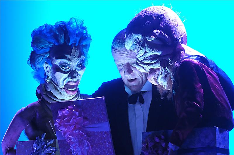 Mrs. Montgomery (links) darf schon mal vorab in eines der teuren Geschenke von Dr. Fischer (rechts) blicken, der seine Gäste damit in Versuchung führt. Geld oder Würde? Egal, wie reich sie schon sind – sie entscheiden sich fürs Geld. Mittendrin wird Sebastian Kautz, der die Figuren führt, ein Teil von ihnen.