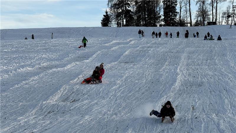 Menschen fahren mit Schlitten den verschneiten Berg hinunter.