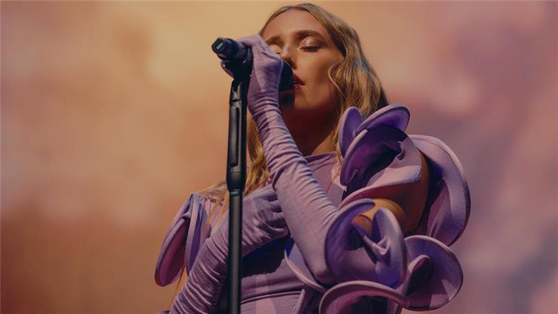 Sängerin mit langen Haaren und auffälligem, voluminösem Ärmelkleid singt vor Mikrofon