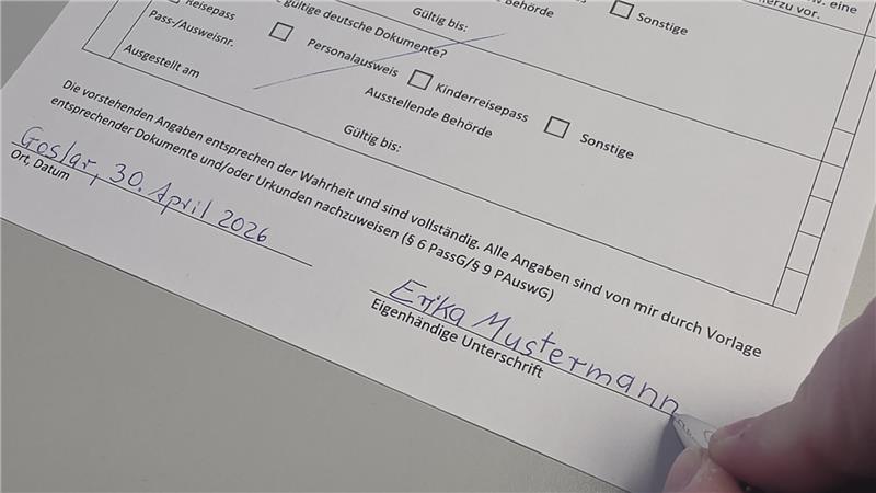 Hand schreibt mit blauer Tinte auf weißem Papier Datum 'Gosler 30. April 2026' und Unterschrift 'Erika Mustermann'.