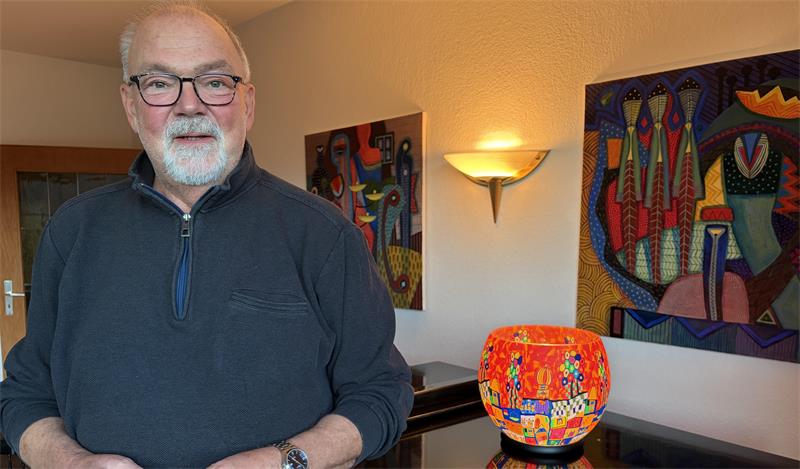 Das Foto zeigt einen Mann vor einem Flügel in seinem Wohnzimmer.