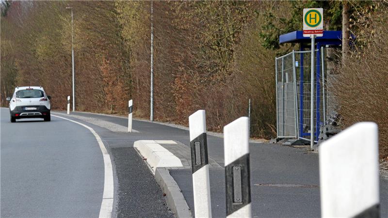 Eine Bushaltestelle an einer Straße, im Vordergrund Leitpfosten.