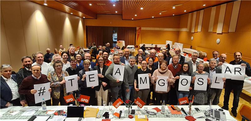 Gruppe von Menschen in einem Saal hält Schilder mit den Buchstaben '#TEAMGOSLAR' hoch