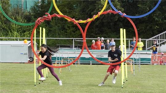 Nach dem Slalomparcour müssen die Kinder Bälle durch die olympischen Ringe werfen.