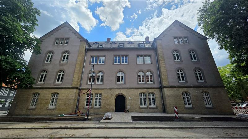 Altes mehrstöckiges Gebäude mit symmetrischer Fassade, mehreren Fenstern und einem zentralen Eingang unter blauem Himmel mit Wolken